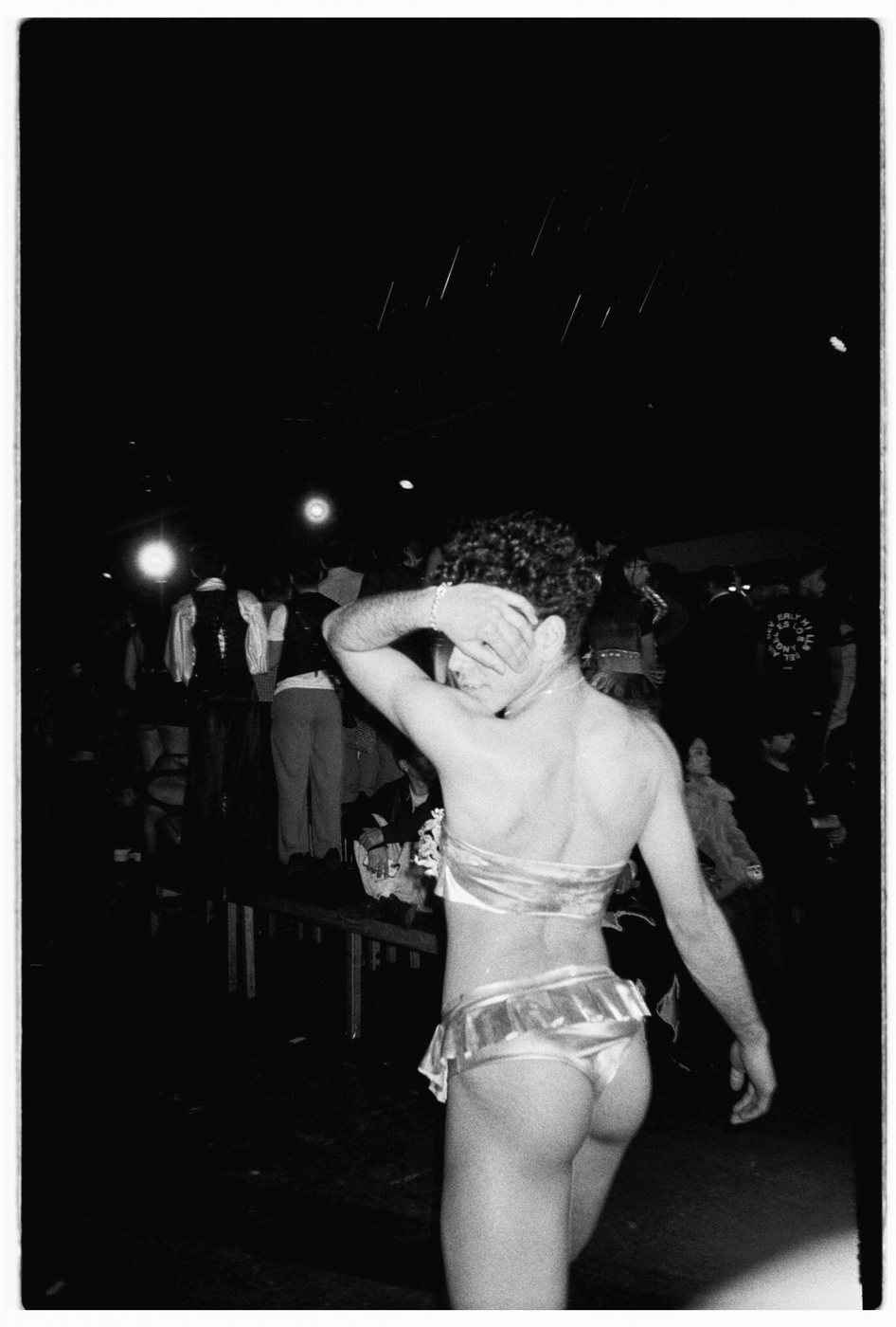 Person in a metallic two-piece walking away, covering their face