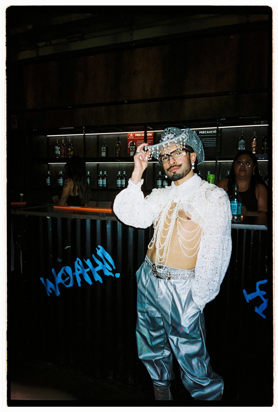 Person in a pearl-covered cowboy hat and silver trousers at a bar