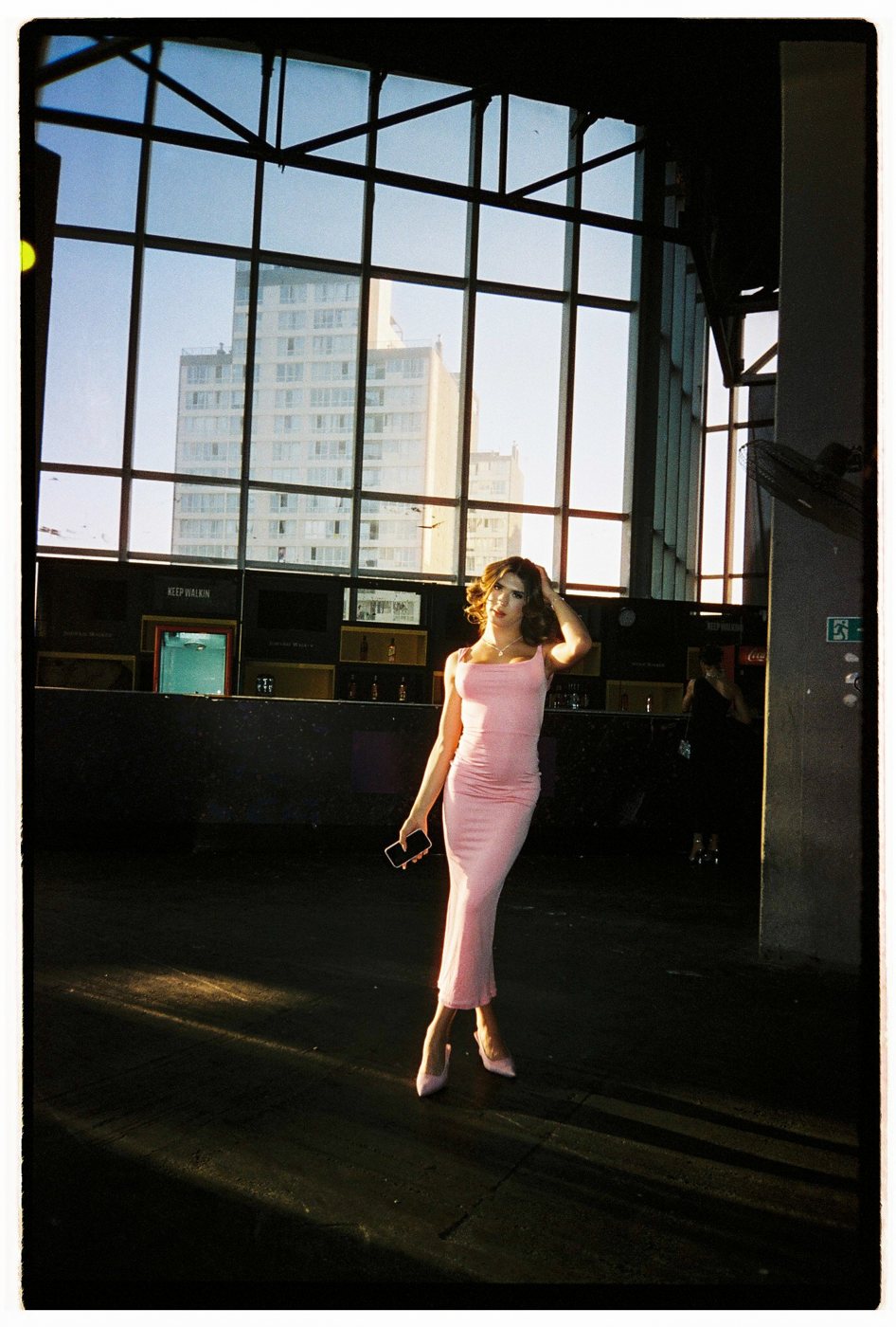 Person in a pink dress standing in sunlight before a tall industrial window