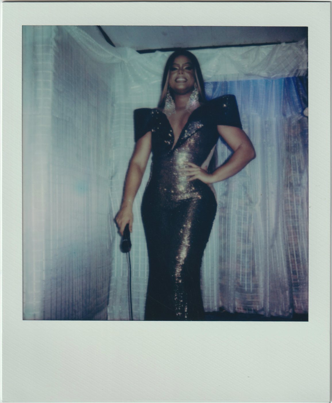 Woman in a sequined gown holding a microphone on a draped stage