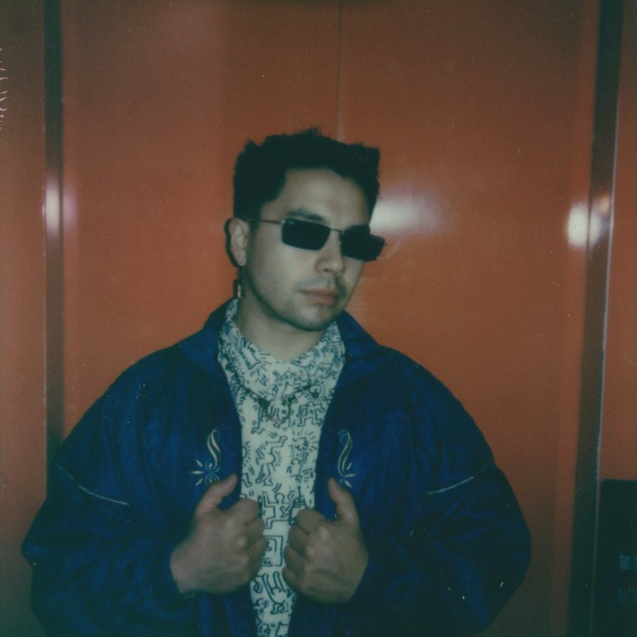 Person in a blue jacket and patterned shirt before an orange door