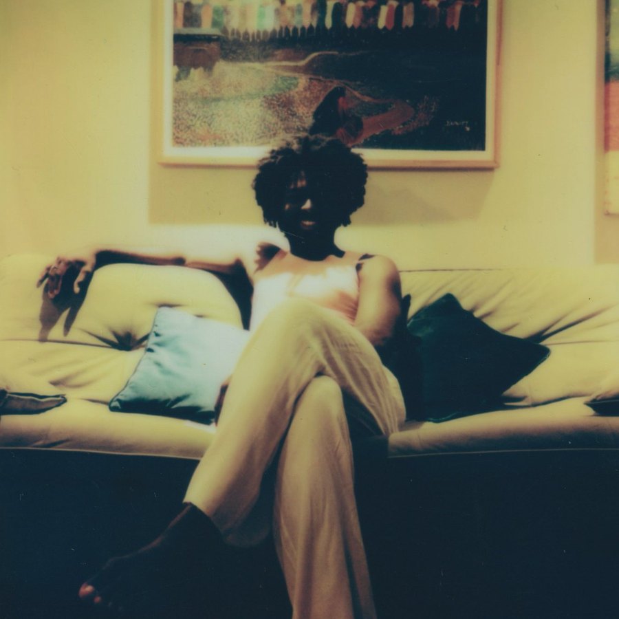 Person seated cross-legged on a cream sofa under a painting