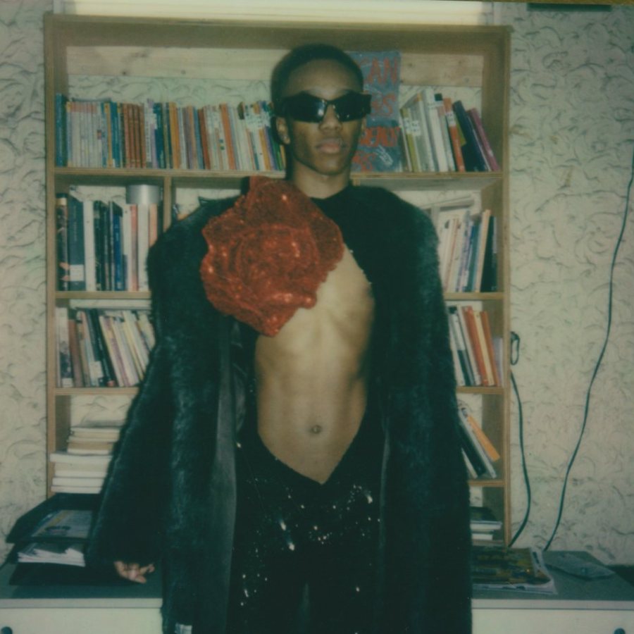Person in sunglasses and a fur coat before a bookshelf